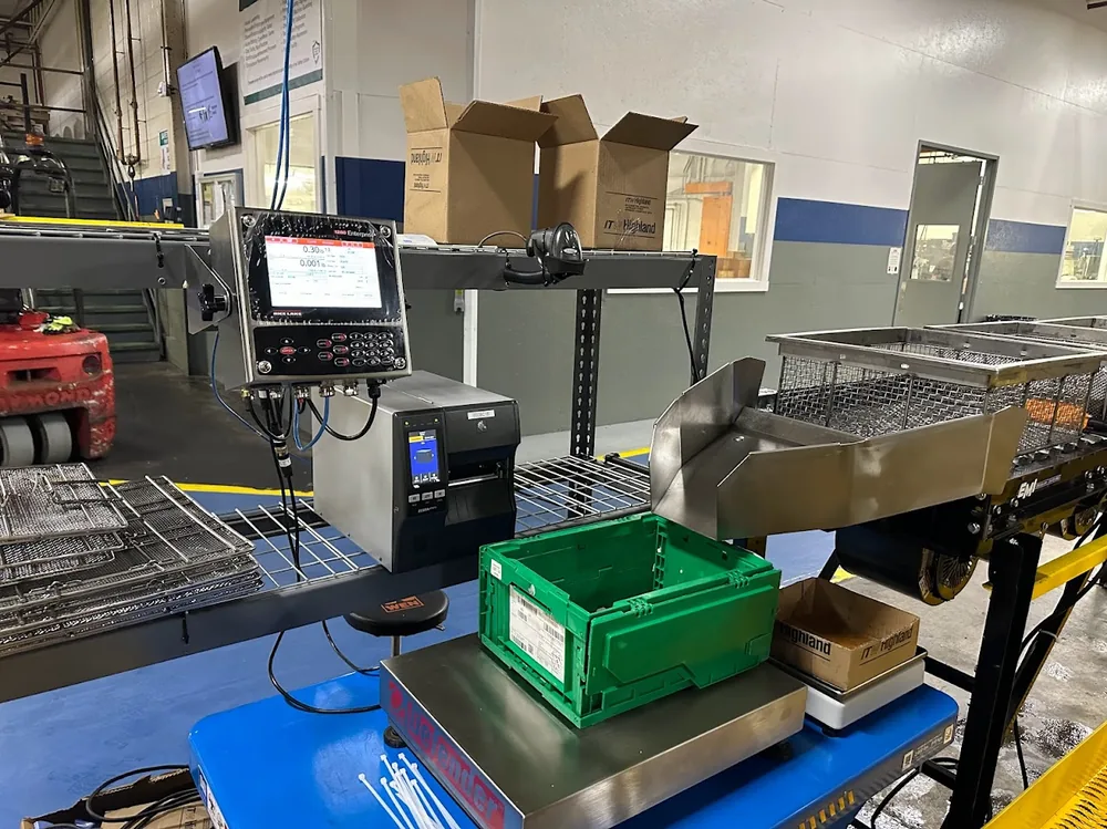 A Rice Lake 1280 Enterprise indicator and Zebra industrial printer mounted over a floor scale weighing a green tote on the plant floor.