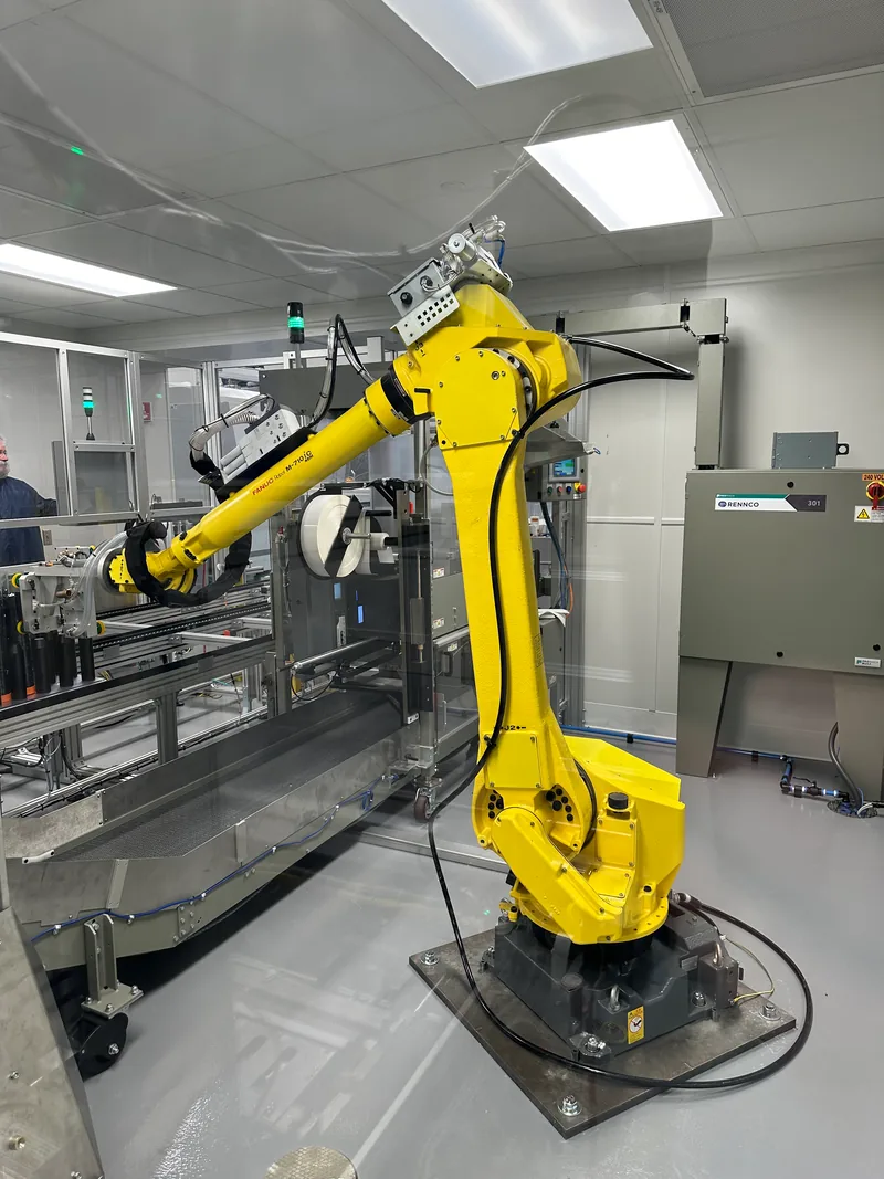 A FANUC robotic arm integrated with a Rennco packaging machine and stainless conveyor in a manufacturing cleanroom.